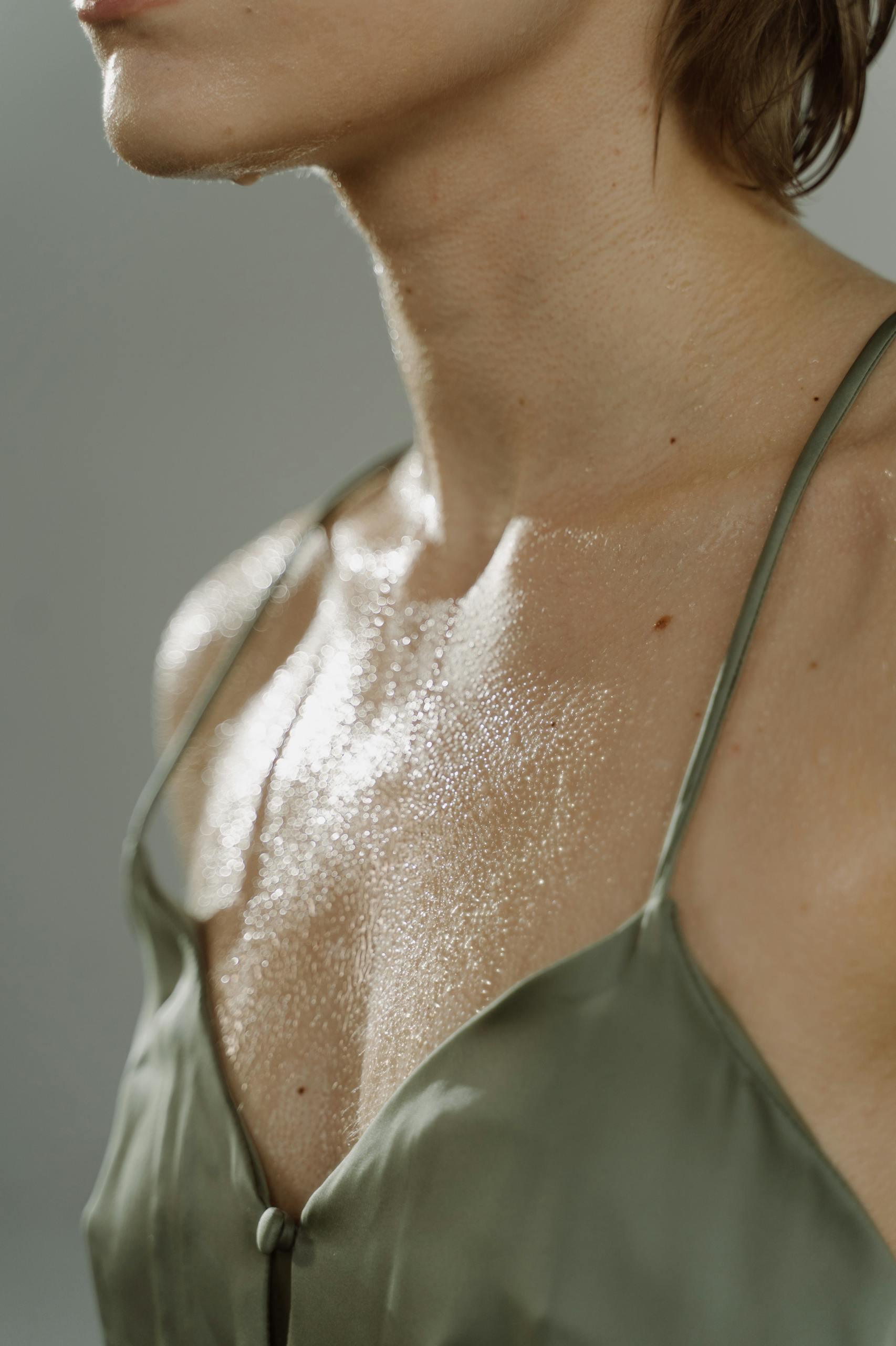 Close-up of a woman's wet chest in a green silk top, highlighting sweat.